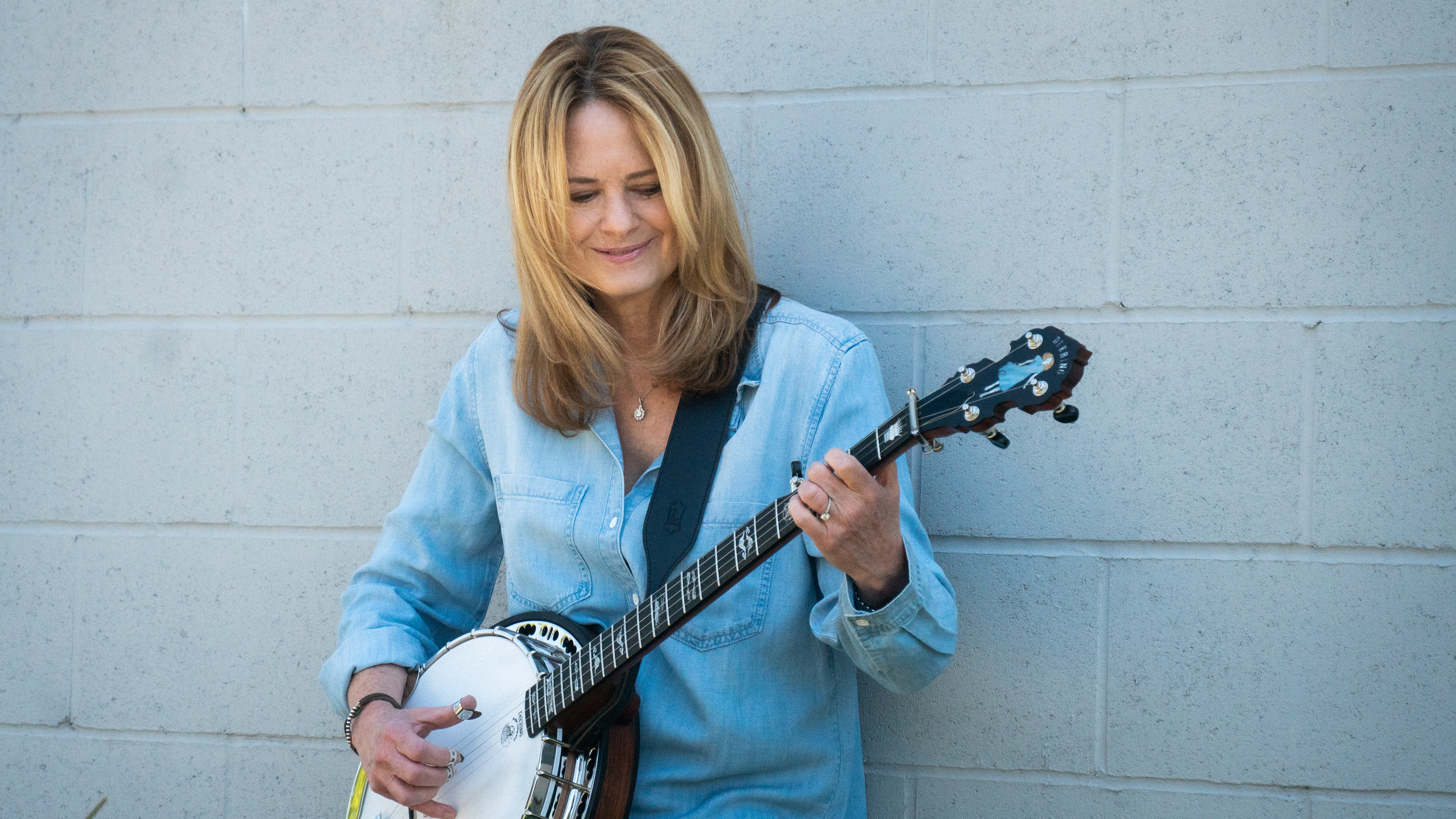 Alison Brown in a denim shirt playing the banjo
