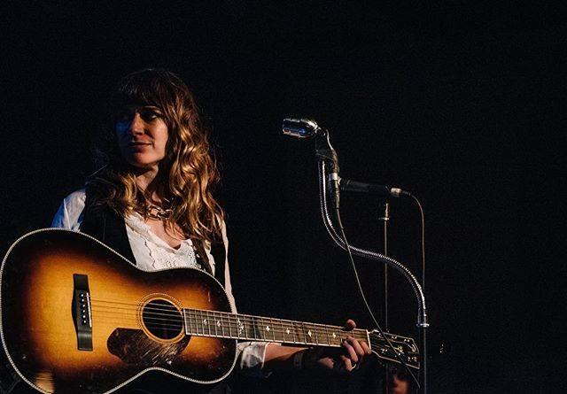 Nicole Atkins in front of a microphone holding a guitar