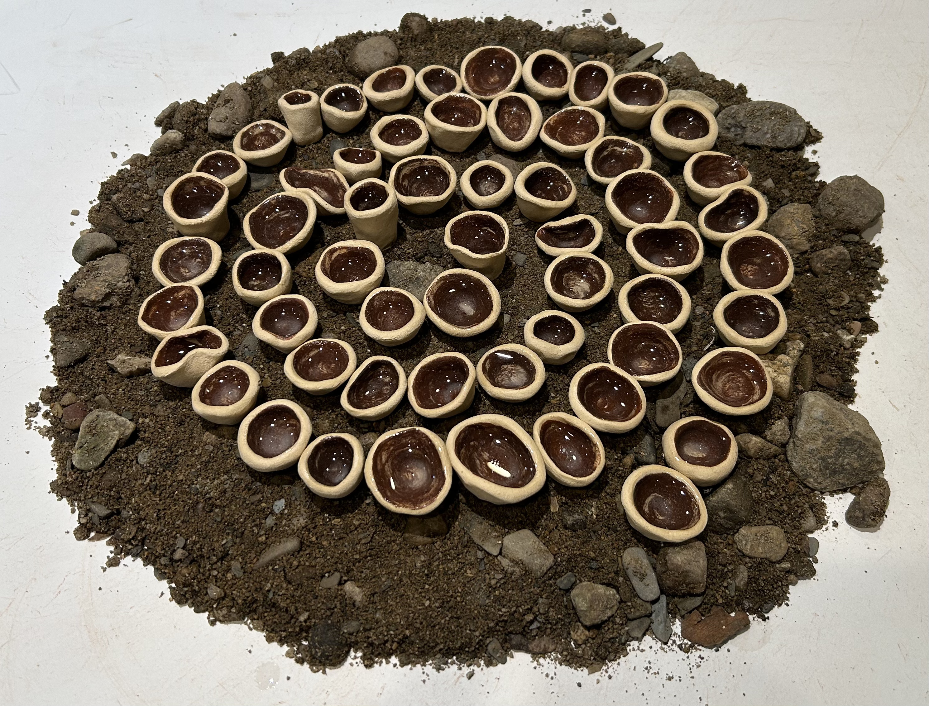 Clay pinch pots on top of dirt and rocks by a window
