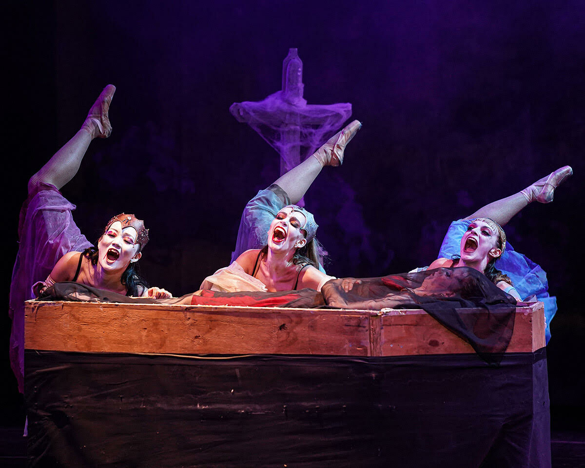 Three dancers performing behind a coffin