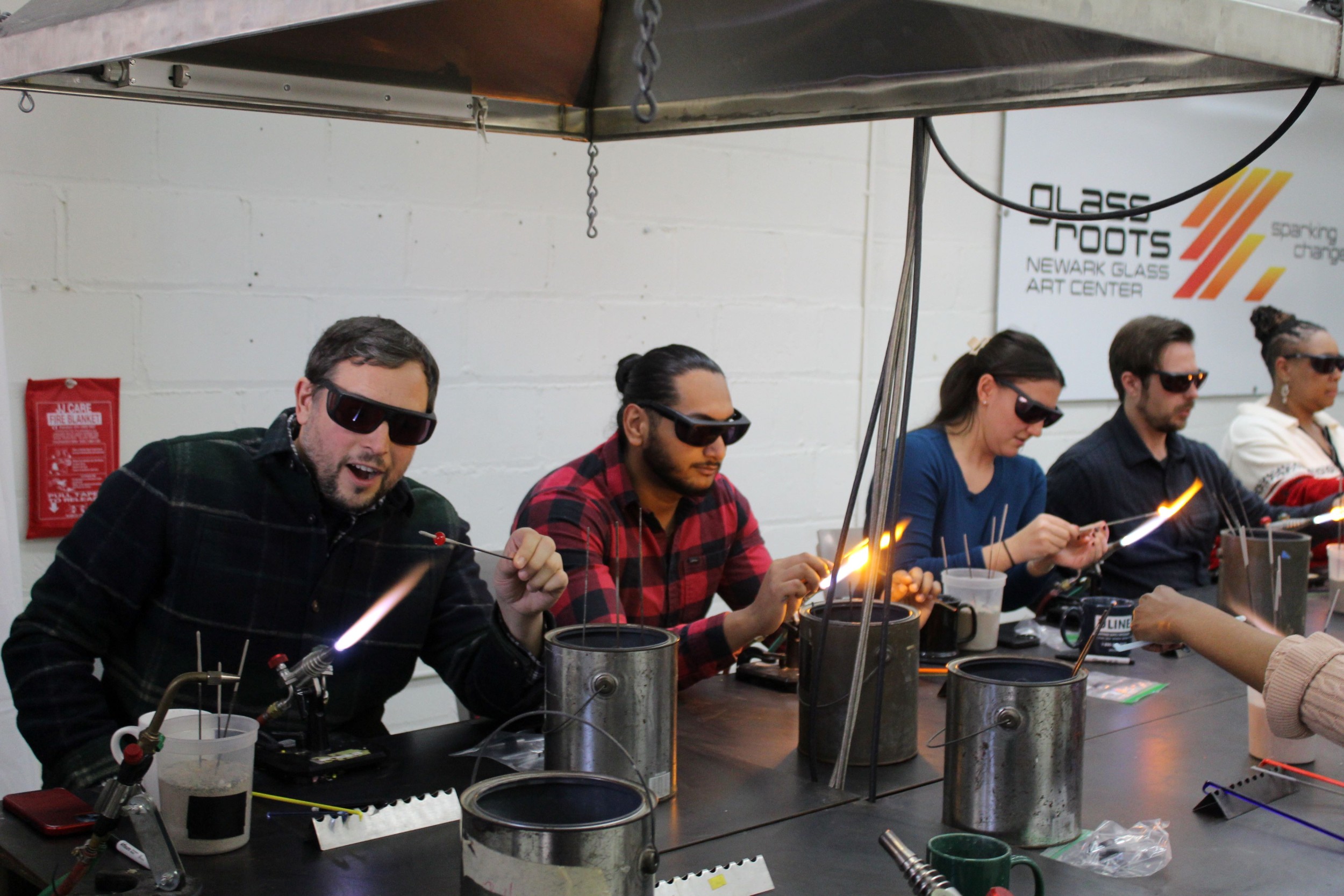 Diverse adult group making beads at a table torch with a surprised look at the flame