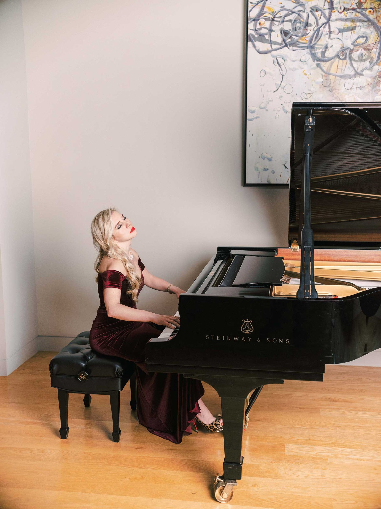 A woman sits at a piano in a studio with her eyes closed while playing.