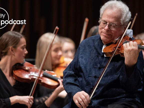 Itzhak Perlman standing, playing the violin, with violinists behind him sitting in chairs