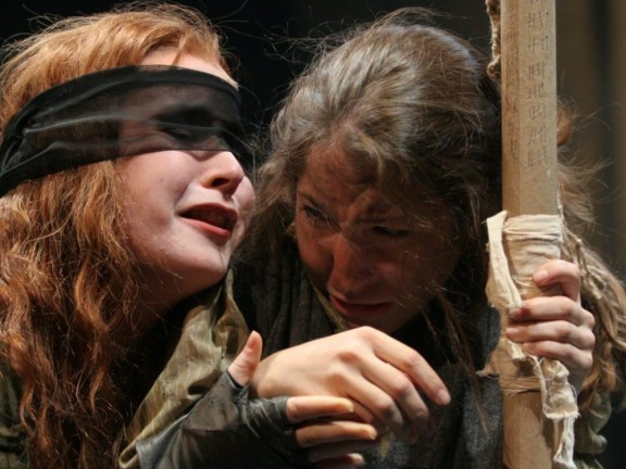 Actor blindfolded next to another actor holding onto a pole
