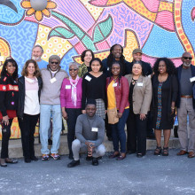 A group of 15 people stand on a street in front of a mural