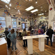 Group of visitors gathered inside an artist studio filled with colorful kinetic sculptures and hanging artwork during an ope