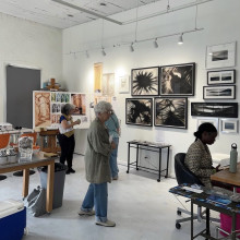Visitors explore a contemporary art gallery featuring framed black and white and mixed media works displayed on white walls.