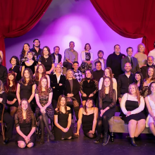 A group of people posing for a photo on stage in front of a red curtain