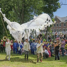 a large puppet of a white bird is operated by three people, showing it off in front of a crowd