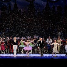 A group of dancers posing onstage with fake snow falling around them