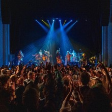 large crowd at indoor concert enjoying a rock and roll show on stage