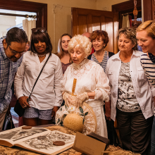 A group of adults on a tour of an old estate pause to admire an old book