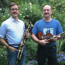 Two men standing in a garden holding a violin and a trumpet