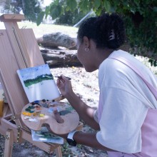 a girl leans over an easel while painting a landscape