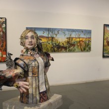 art depicting woodland creatures and young blonde women displayed in a gallery with white walls and grey flooring
