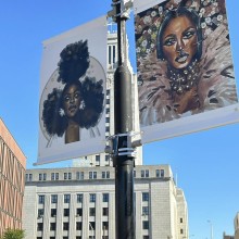 Two paintings of African American women displayed on a city street lamppost