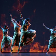 a group of dancers wearing traditional south Asian costumes on a blue stage
