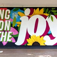 mural with groovy text saying “bring on the joy” on a background of colorful flowers