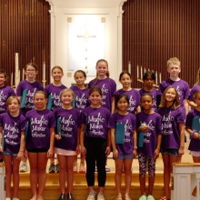a choir of children wearing matching purple shirts posing for a photo in front of two microphones