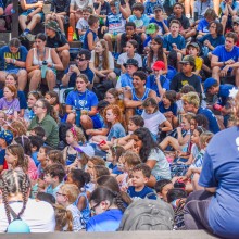 outdoor bleachers filled with children at summer camp all wearing blue and spectating some event