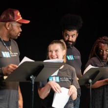 A group of people standing in front of their scripts rehearsing something