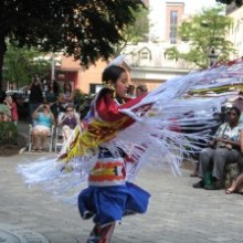 A woman in a feathered dress performs a dance in front of a crowd