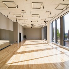 A sunlit empty room with a wall of mirrors, wooden floors, and large windows of the rehearsal room at NBPAC