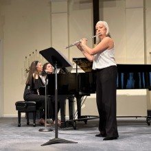 A woman playing a flute in front of a piano