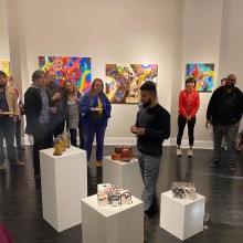 an artist stands among their work in a gallery while spectators look on