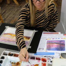 A woman painting a watercolor of trees in the winter at sunset