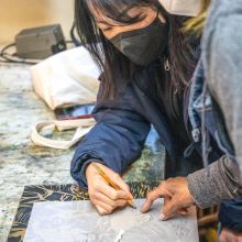 Two women wearing face masks trace over an image of a woman together