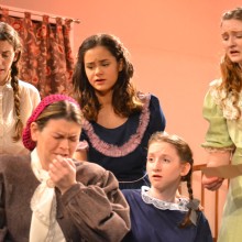 Actresses perform a scene from Little Women on stage in costume