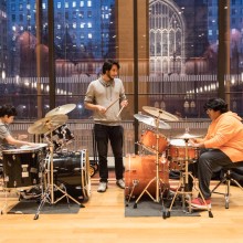 Two boys sitting in front of drum sets and practicing under the guide of a teacher