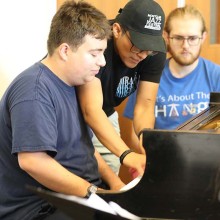 Two young men sitting in front of a piano being guided by a teacher