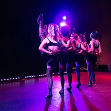 A line of women on stage in all black costumes doing high kicks