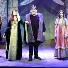 A performance onstage of play set in medieval times, a king and queen in the center stage with their royal court around them