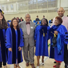 A group of college faculty in blue regalia gowns smiling at a graduation ceremony