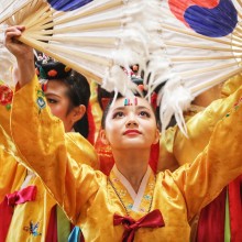 A woman in a yellow dress holding fans with the Korean flag on them