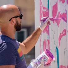 man paints pink and blue on a shipping container
