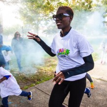 a woman in sunglasses participates in a color run, running through blue powder