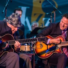 Two men playing guitars on a stage