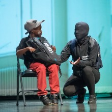 Performance, including a child and person in a full face-covering mask
