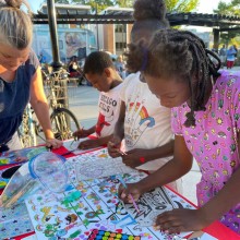 Children and a woman working on artwork at a table with supplies and stickers