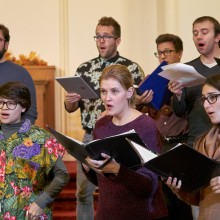 The Glassbrook Vocal Ensemble holding their songbooks singing in a rehearsal