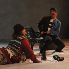 an actor sitting on a park bench yells at another actor portraying a homeless man crawling towards him