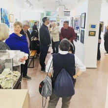a group of older people fill an art gallery, looking at the various artworks hung on the walls