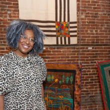 Artist smiling in front of her textile artwork hung up in Camden FireWorks