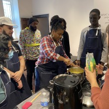 A group of people observe a woman preparing food