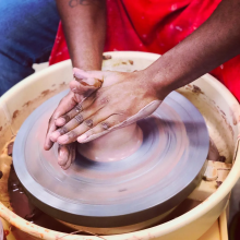 An image of hands over a clay wheel, working on a piece of clay