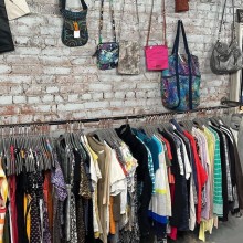 A rack of clothes and purses hanging on a grey brick wall